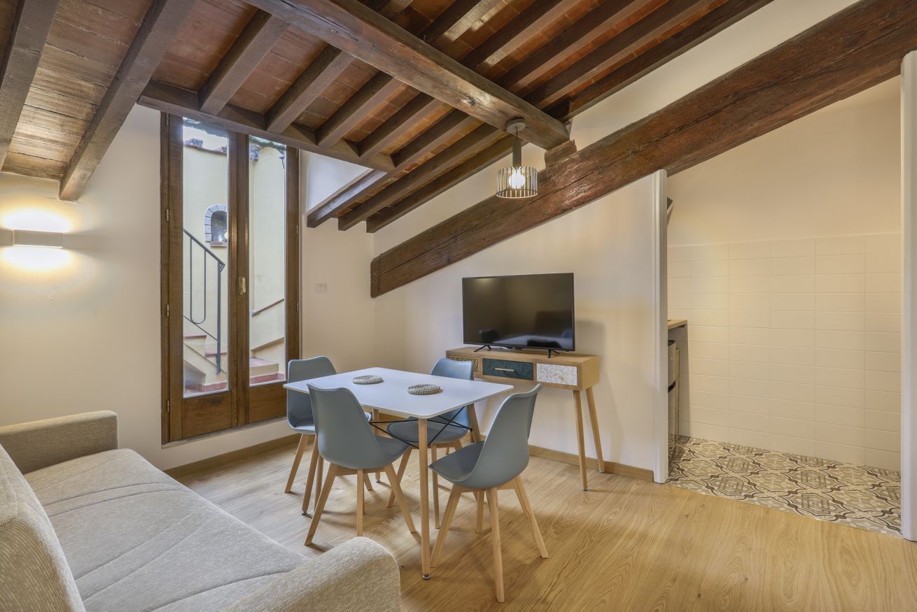 Un salon moderne comprenant un coin repas, des poutres en bois, un téléviseur à écran plat et un escalier.