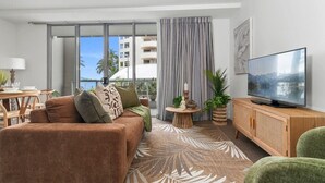 Una sala de estar moderna con un sofá, televisor y vistas a un edificio a través de amplios ventanales.