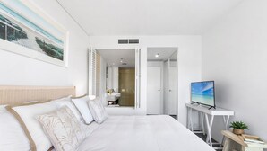 A hotel room with a large bed, a TV, a small desk, and a bathroom visible through an open door. - Waterfront Oasis with Pool, Gym and Sauna in Cairns (Cairns City)