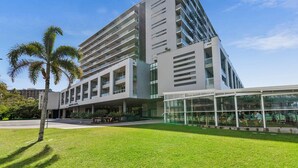 A modern building with multiple floors, large windows, and a covered outdoor seating area. - Waterfront Oasis with Pool, Gym and Sauna in Cairns (Cairns City)