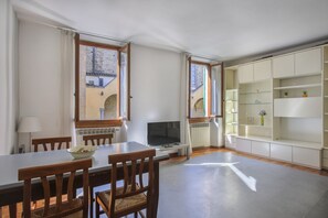 Een eethoek met een tafel, stoelen, een televisie en uitzicht op een gebouw door een raam.