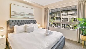A hotel room with a large bed, a view of the outside balcony, and a painting on the wall. - Tropical Retreat with 9 Pools Gym and BBQ Access (Westcourt)
