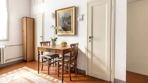 A dining area with a wooden table and chairs, a vase with flowers, and a framed picture on the wall.