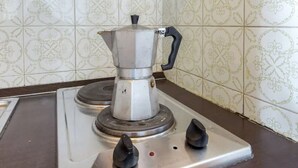 A kitchen with a gas stove, a coffee pot, and patterned tiles.