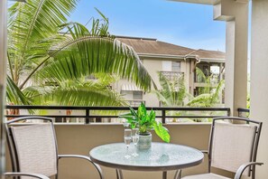 A round glass table with two chairs on a balcony, a potted plant, and a clear view of a building with a tiled roof. - Tropical Resort Apartment with 9 Pools and Gym (Westcourt)
