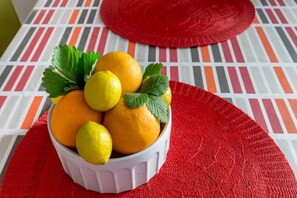 Un saladier rempli d’oranges et de citrons, avec quelques feuilles, posé sur une table recouverte d’une nappe à rayures.