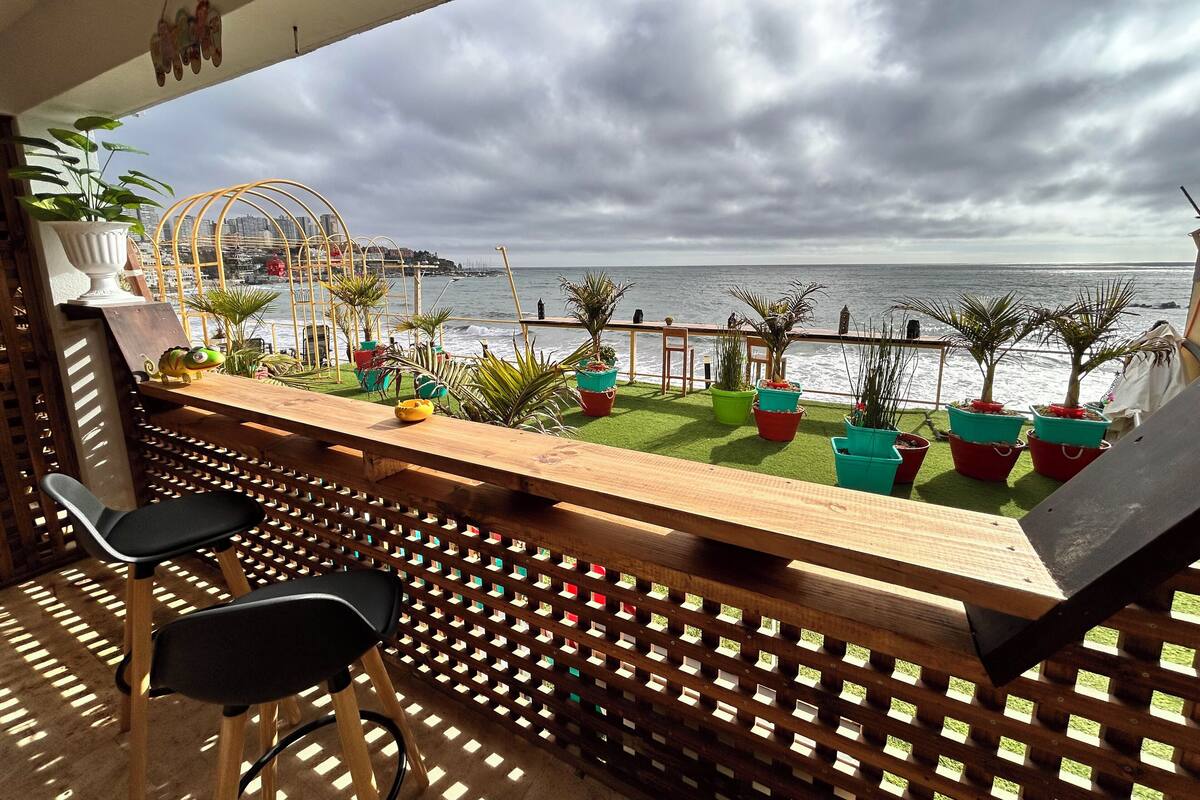A balcony with a view of the sea, potted plants, and a wooden table with chairs.