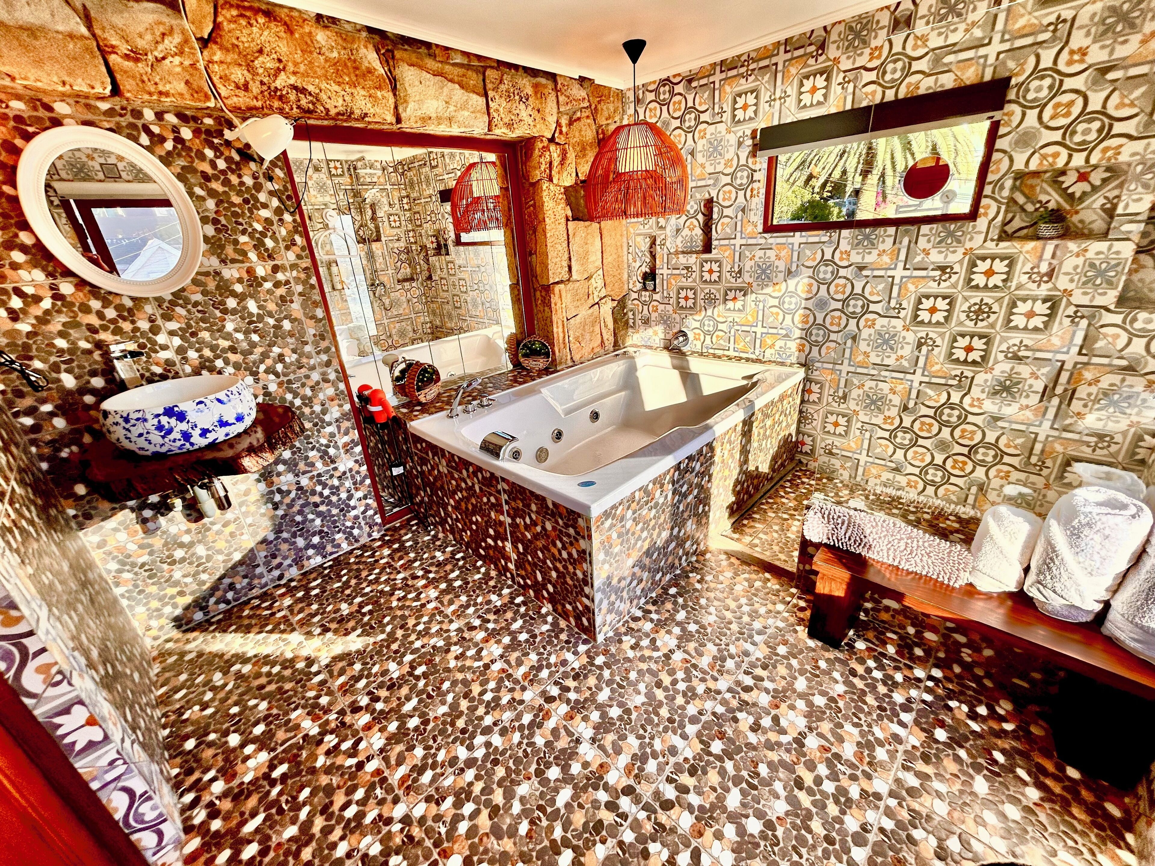 Une salle de bain avec un mur en pierre, une baignoire, un lavabo agrémenté d’un récipient à motifs floraux bleus et un miroir.