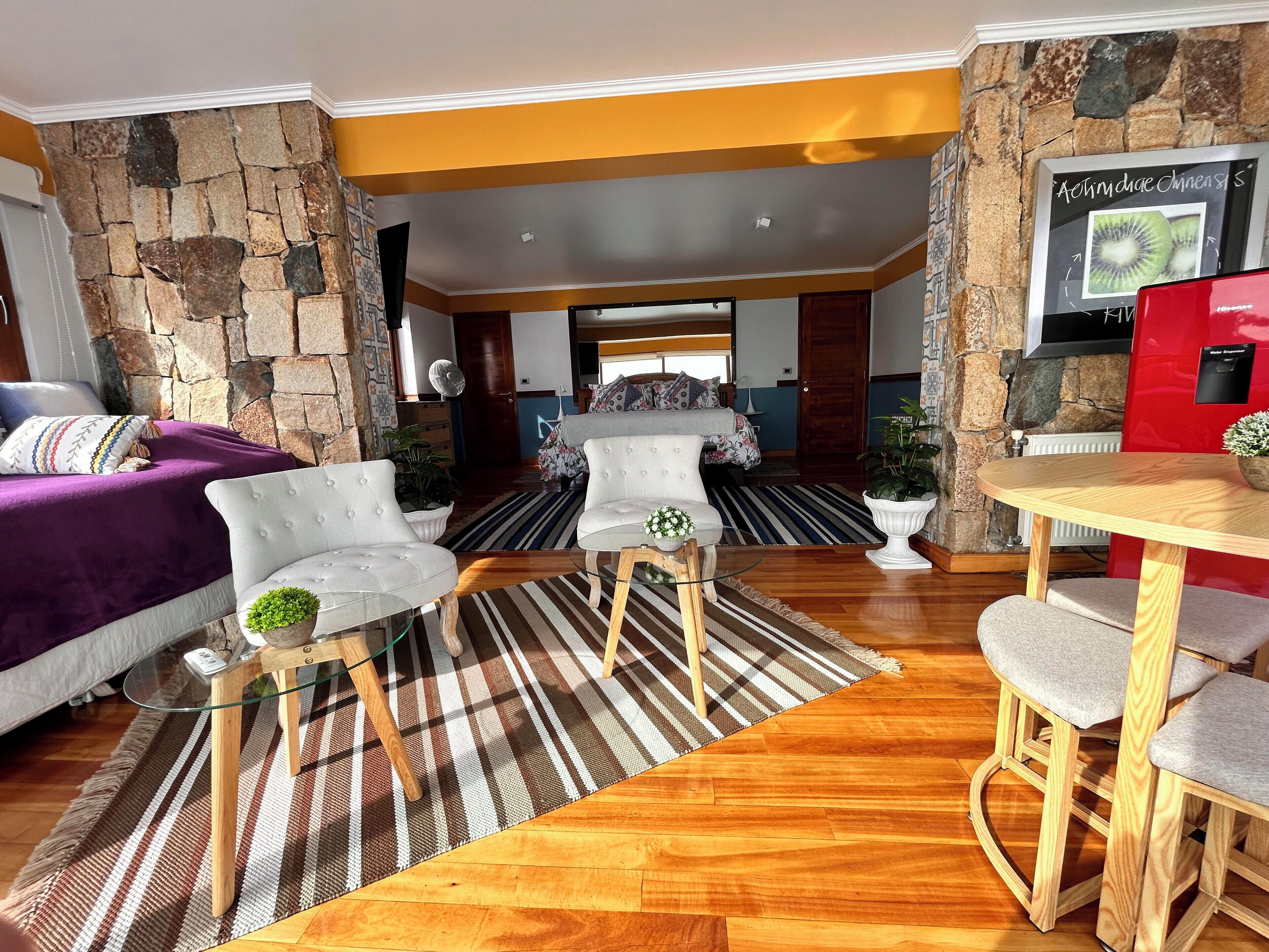 A modern living room with a stone wall, a wooden floor, and a dining area with a red appliance.