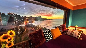 A room with a large window overlooking a cityscape at sunset, a bed with multiple pillows, and a small table with a vase. - PACIFICSUNSET CONCÓN (Concon)