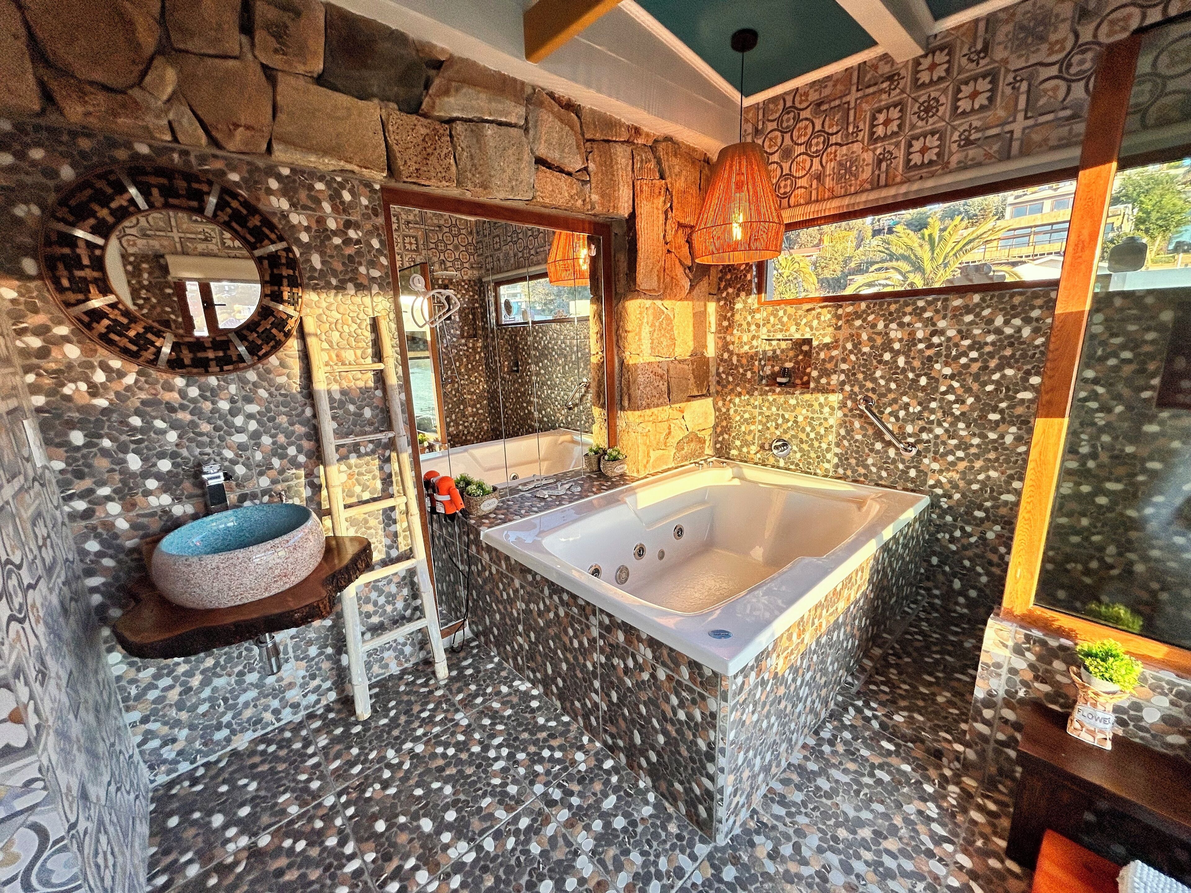 A bathroom with a stone wall, a bathtub, a sink, and a mirror.