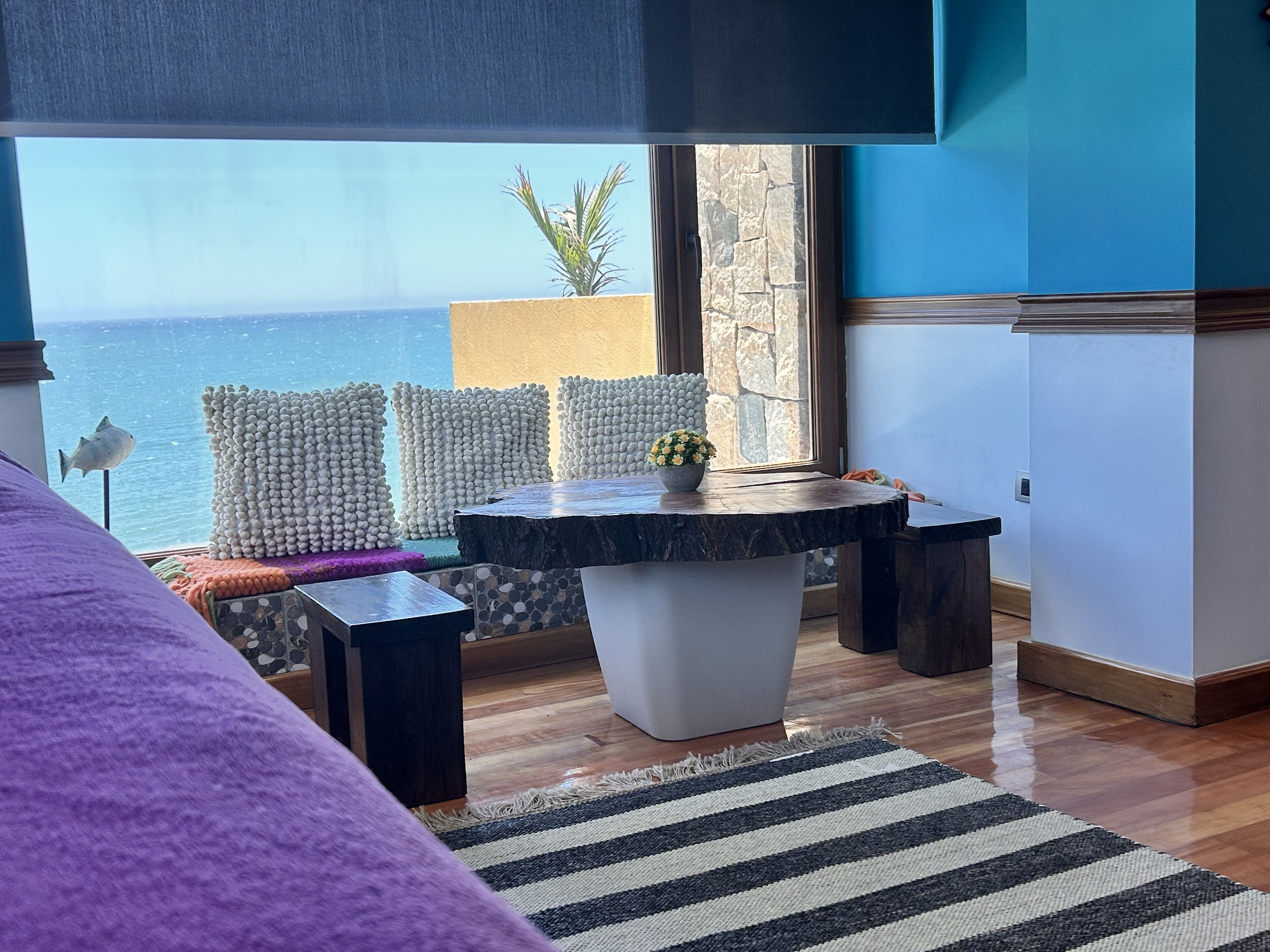 A room with a view of the sea, a round table with a plant, and a purple sofa.