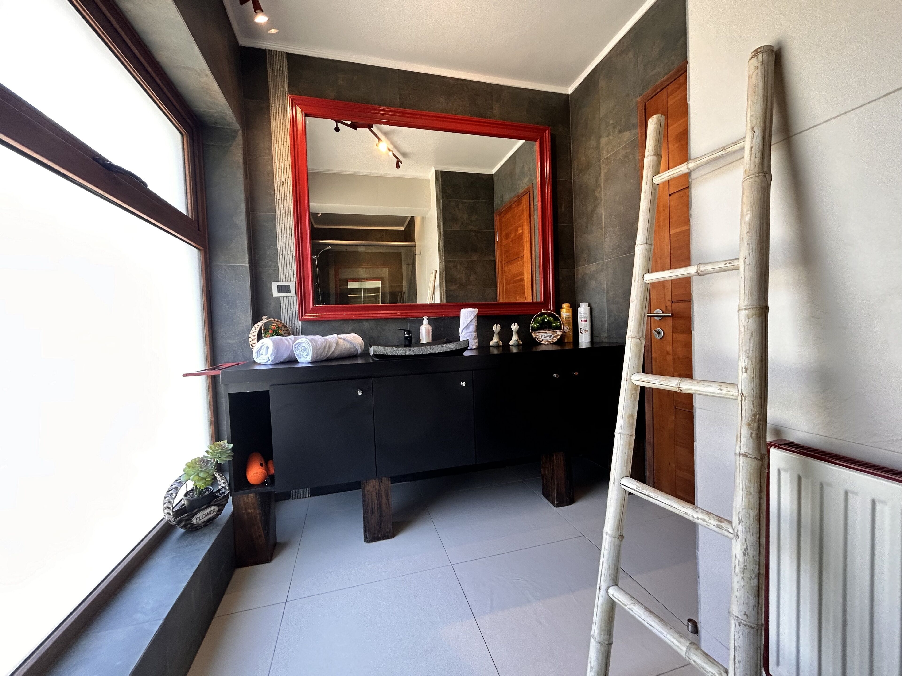 A modern bathroom with a black vanity, a large mirror, and a wooden door.