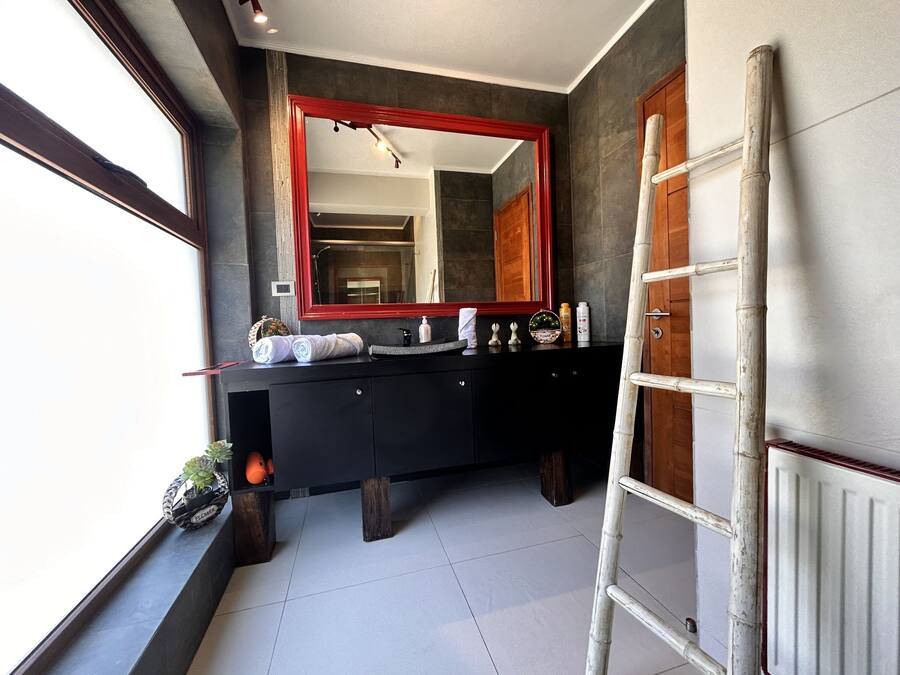 A modern bathroom with a black vanity, a large mirror, and a wooden door.