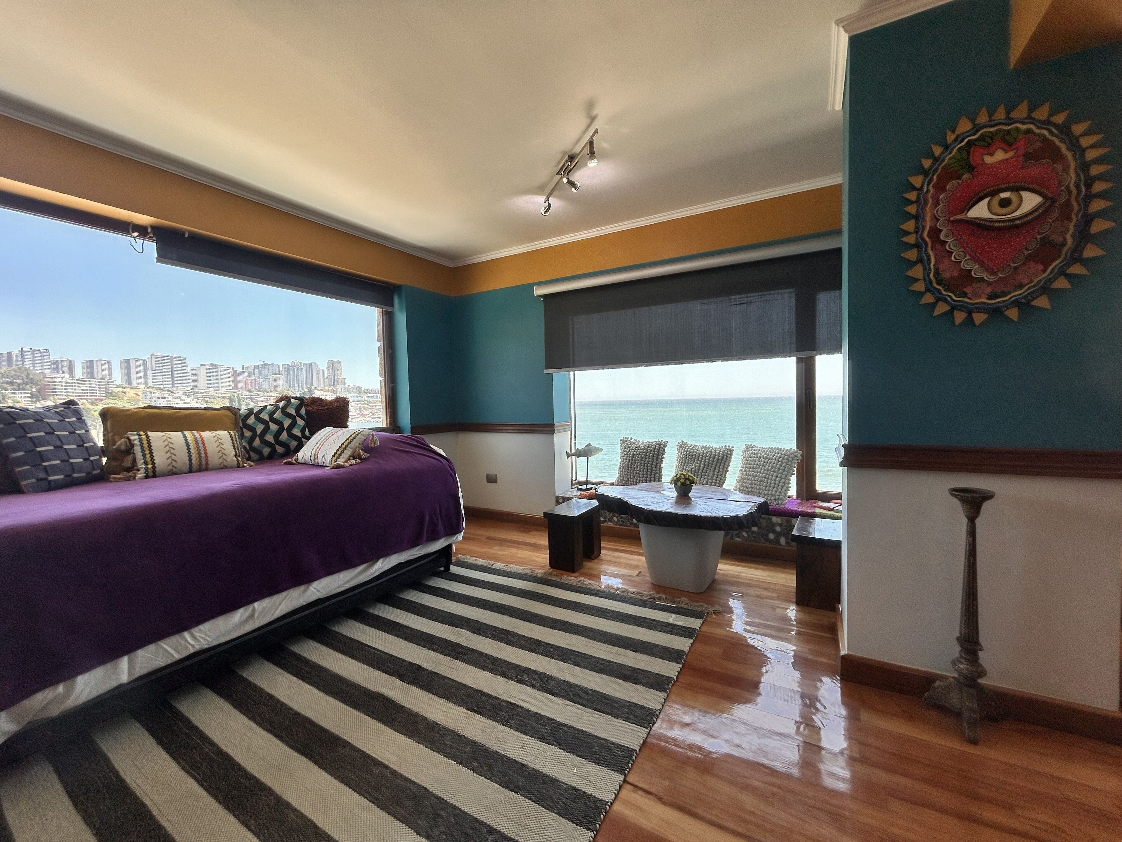 A modern bedroom with a bed, a view of the city, and a decorative wall piece.