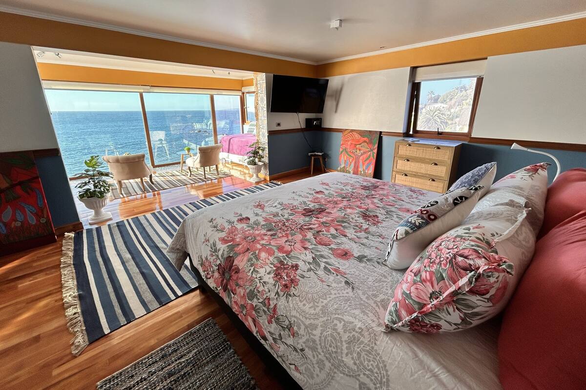 A bedroom with a large bed, a TV, a dresser, and a view of the ocean.