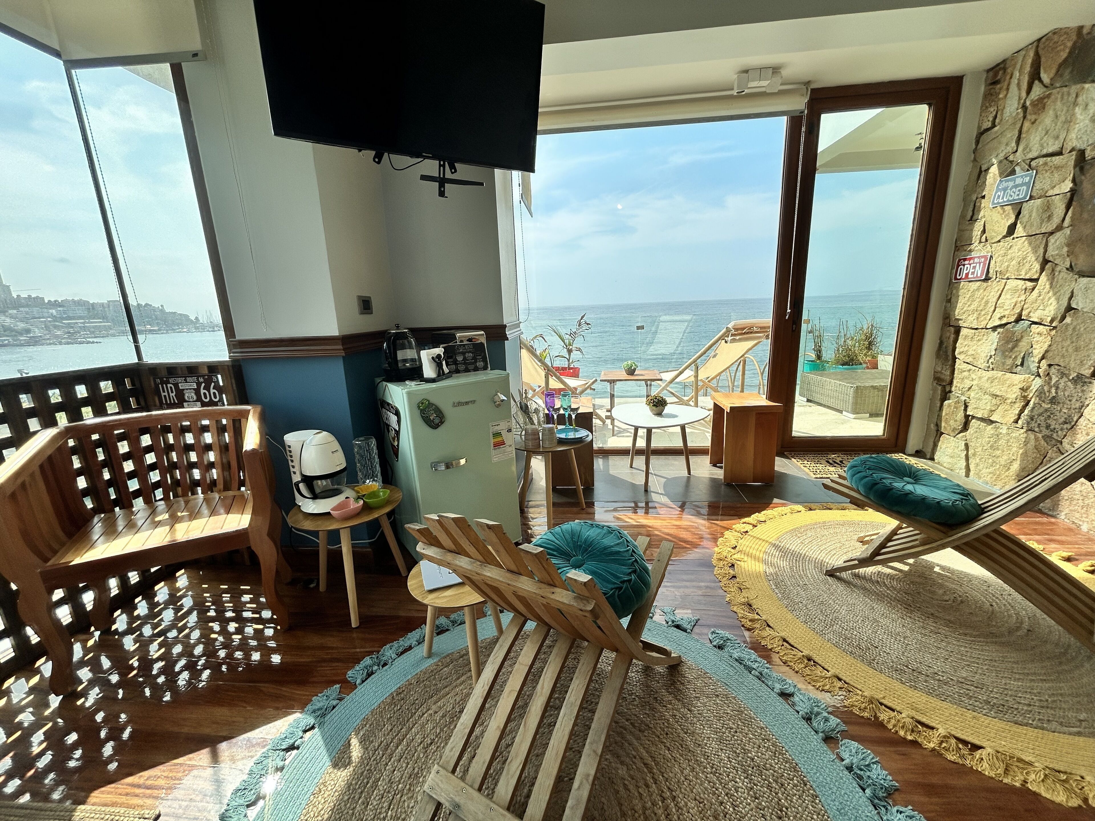Ein Balkon mit Meerblick, ausgestattet mit Holzstühlen und einem Tisch, sowie ein Kühlschrank.