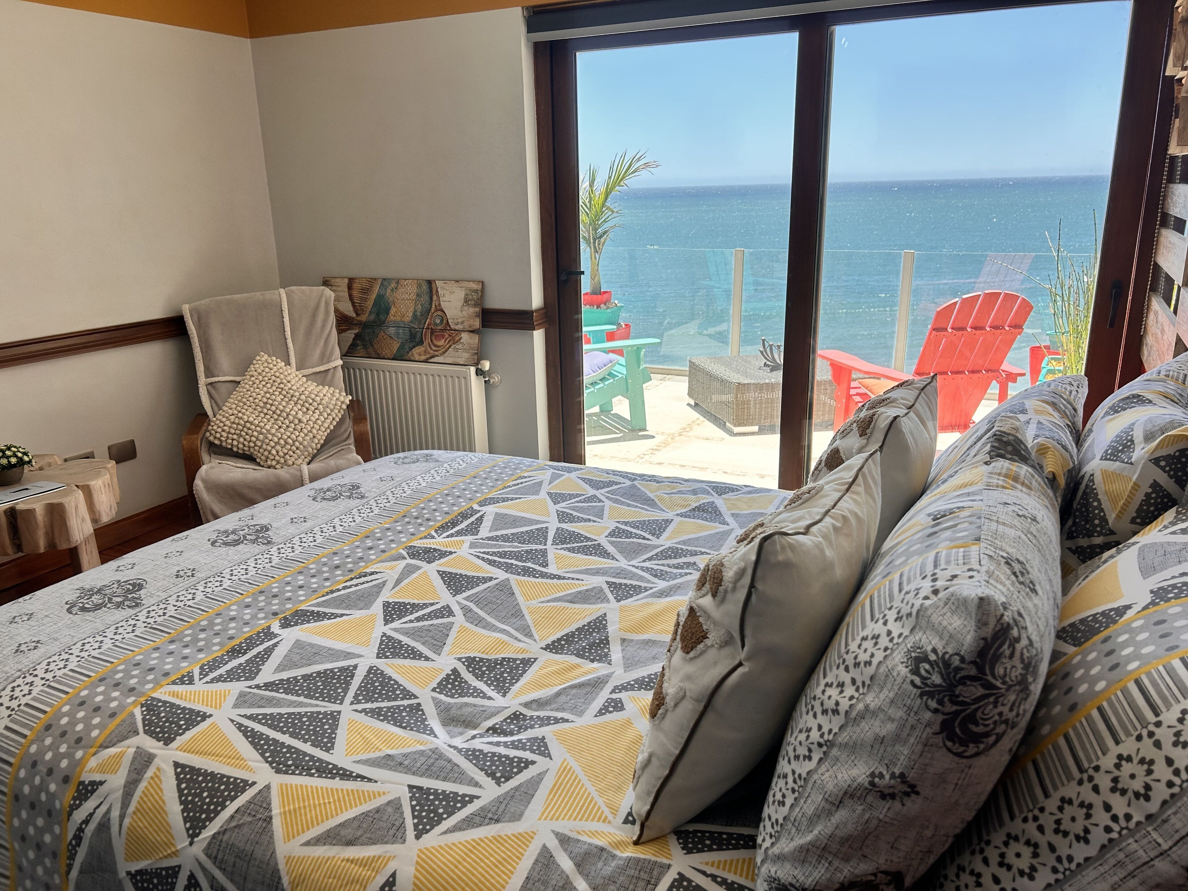 A bedroom with a large bed, a chair, a table, and a view of the ocean.