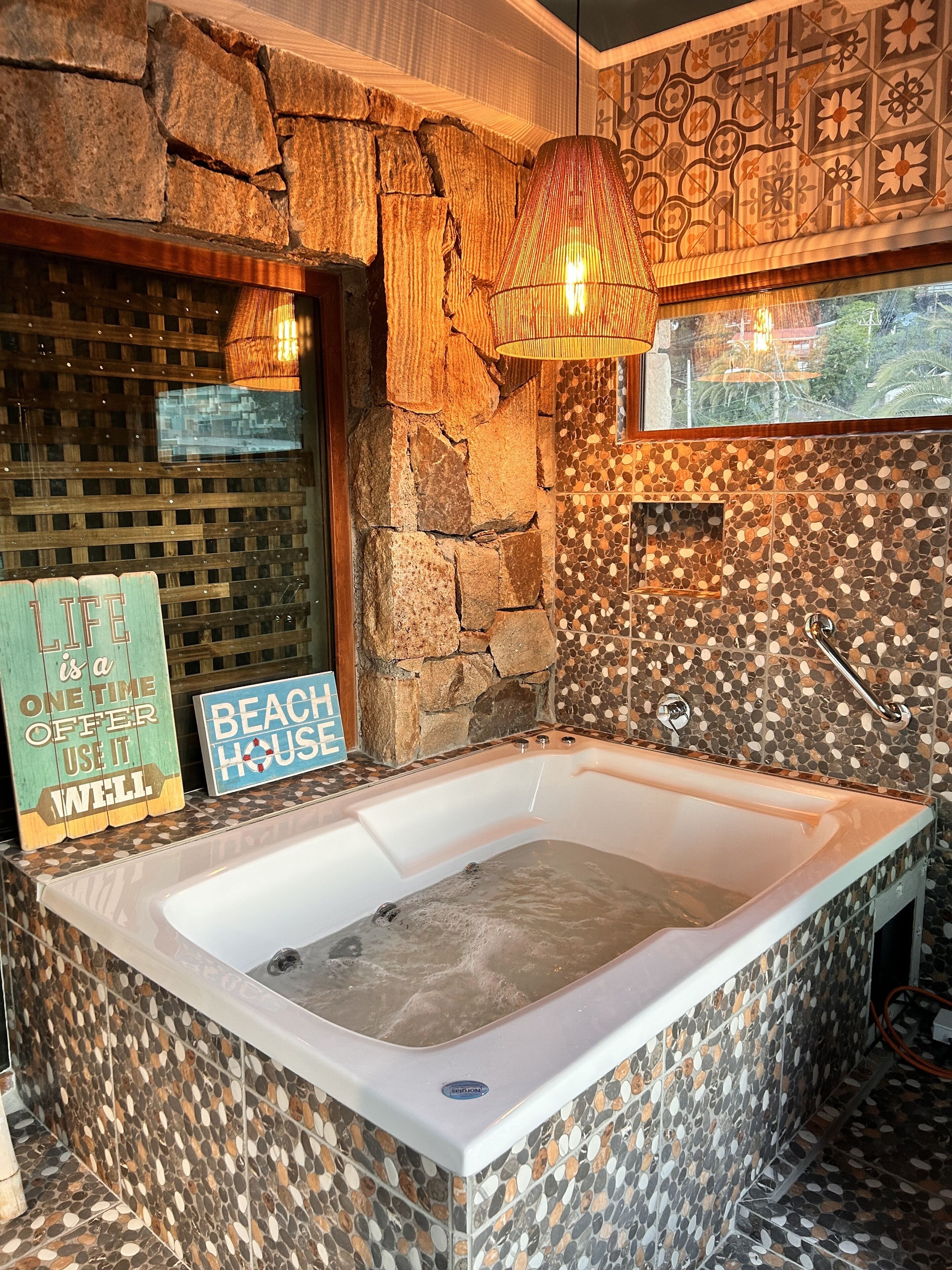 A bathroom with a stone wall, a bathtub, and a mosaic tile design.