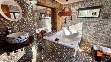 A bathroom with a large oval sink, a freestanding bathtub, and a mirror. The walls are decorated with patterned tiles, and there is a window providing natural light.