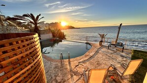 A poolside area with a view of the sunset over the water, a wooden fence, and outdoor seating. - PACIFICSUNSET CONCÓN (Concon)