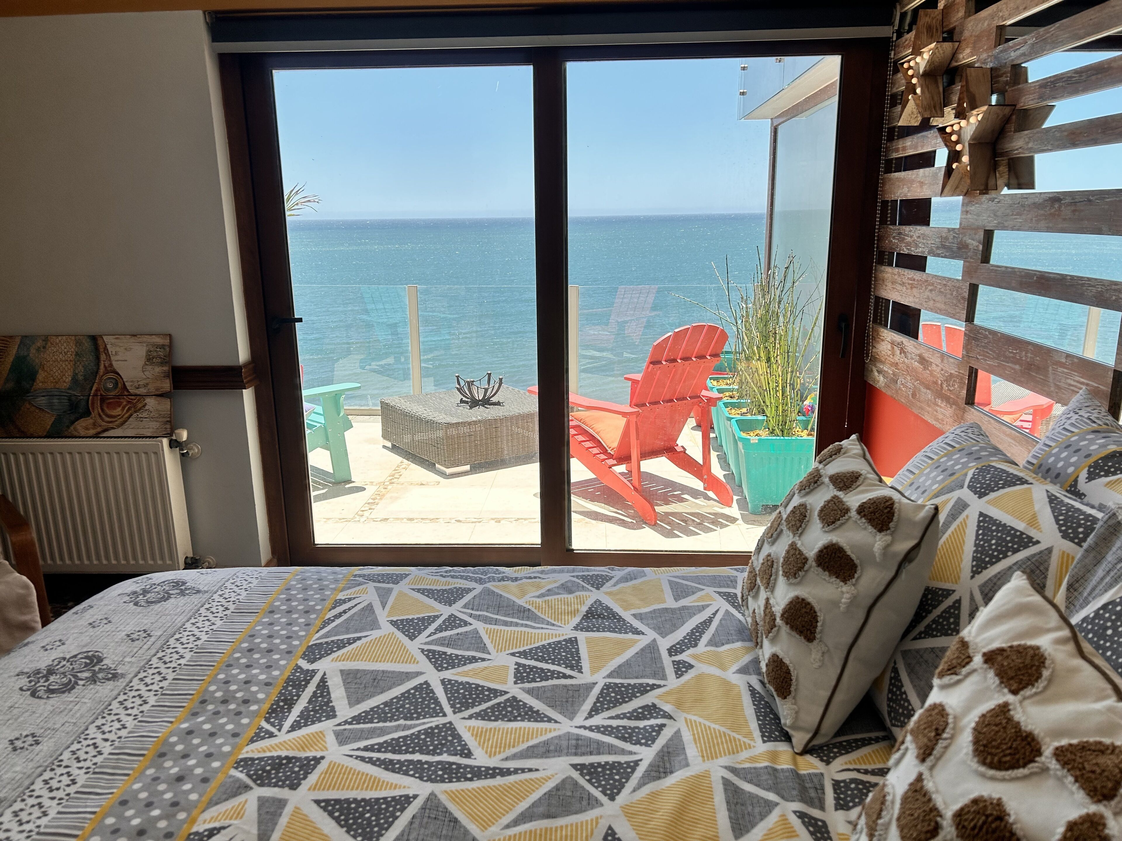 Ein Schlafzimmer mit Meerblick, einem Bett mit gemusterten Textilien und einem Holzkopfende.