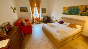Una habitación de hotel con cama, escritorio, silla, una mesita y una estantería.