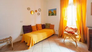 Una habitación con sofá cama, una silla, un cuadro y una ventana con cortinas.