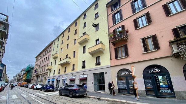 Calle con tranvía, edificios de varios pisos y locales comerciales, incluyendo una farmacia.