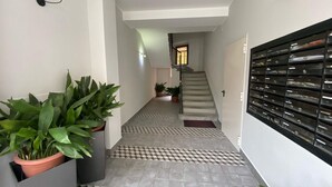Un pasillo con plantas en macetas, una escalera y un mueble de almacenamiento fijado a la pared.