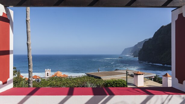 Blick auf die Küste von einer überdachten Terrasse mit rotem Boden, mit Blick auf das Meer und eine Klippe.