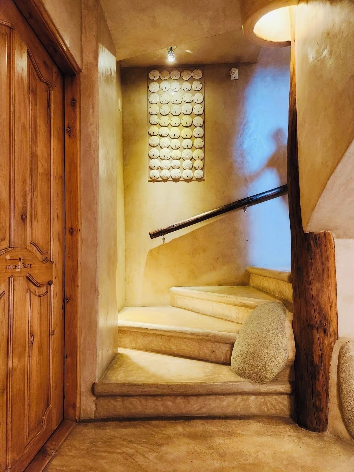 A wooden staircase with a handrail, a wall-mounted clock, and a wooden door labeled "HUICHOL SUITE".