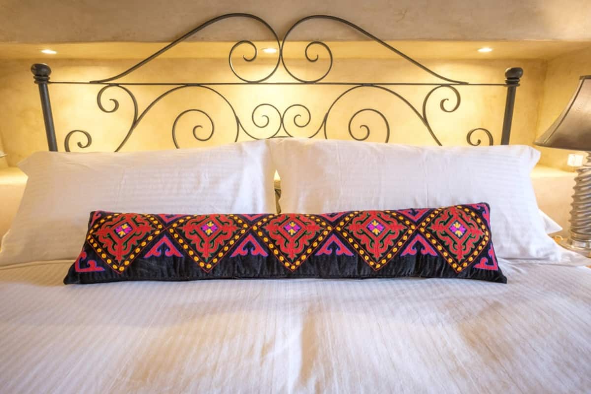 Een bed met witte lakens en een sierkussen met een geometrisch patroon.