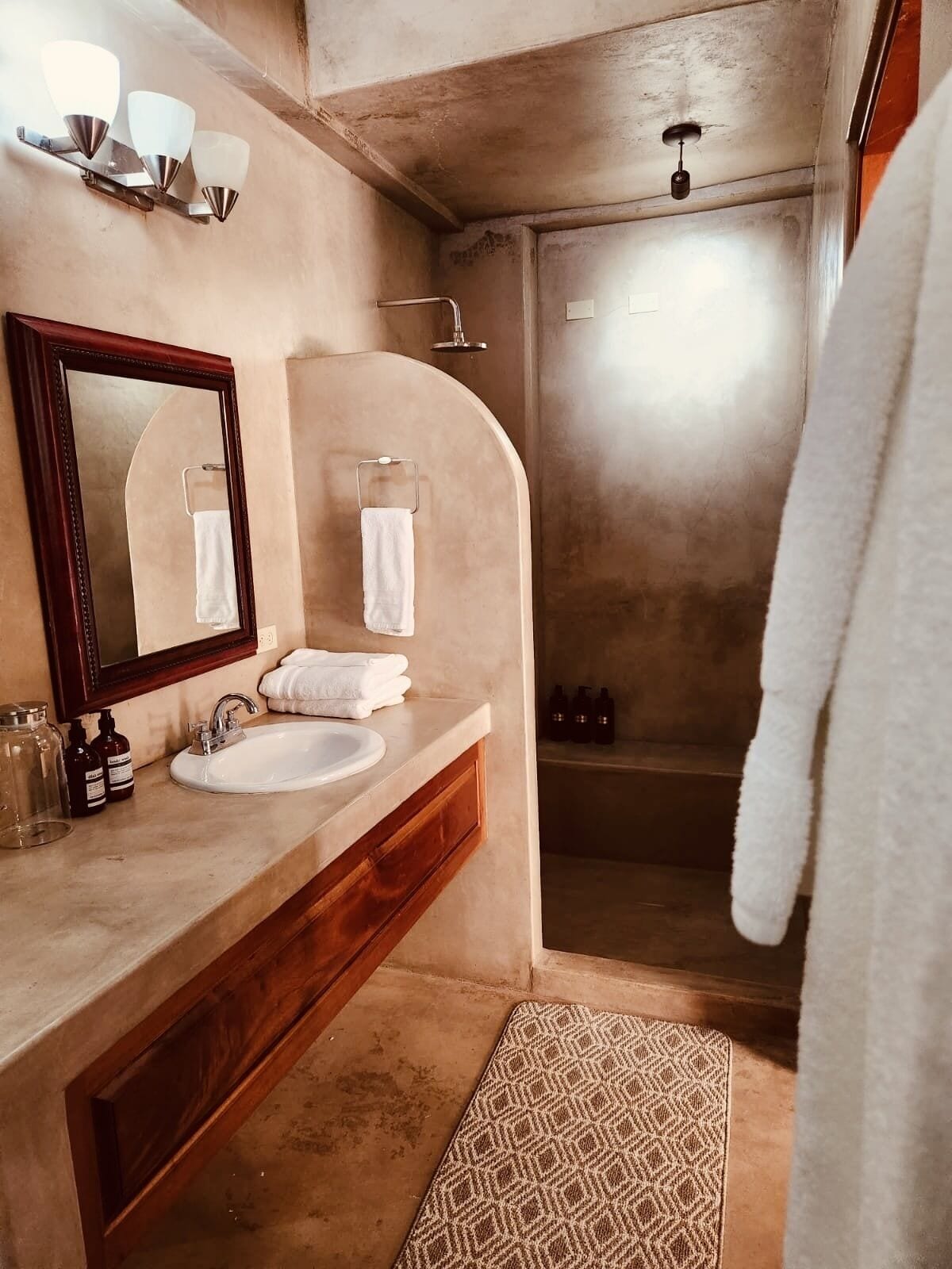 A bathroom with a vanity, mirror, towel rack, shower, and patterned rug.