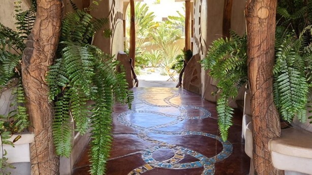 A hallway with a mosaic floor, wooden columns, and ferns. - Alegria Suites Centro Historico  (Todos Santos)