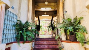 A grand staircase with ornate railings and potted ferns, leading to an arched entrance. - Alegria Suites Centro Historico  (Todos Santos)