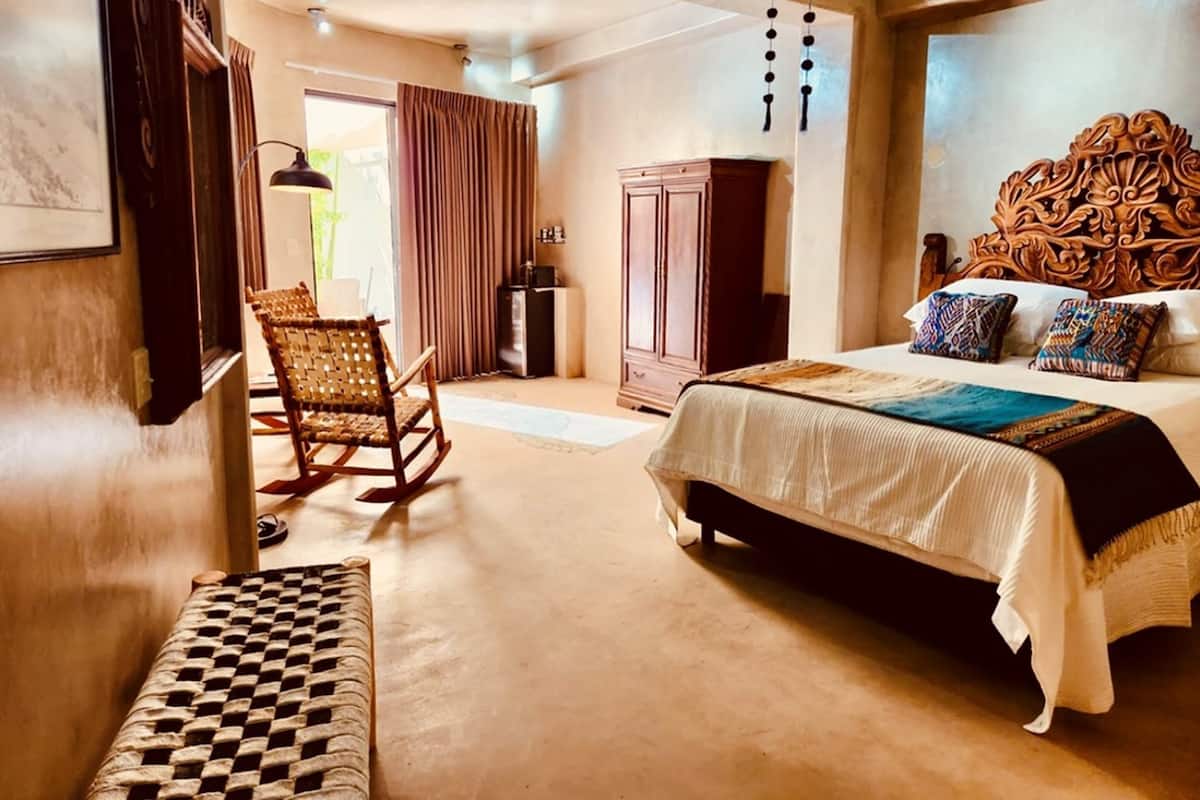 Een slaapkamer met een groot bed, een houten hoofdbord, een schommelstoel, een kledingkast en een geruit tapijt.