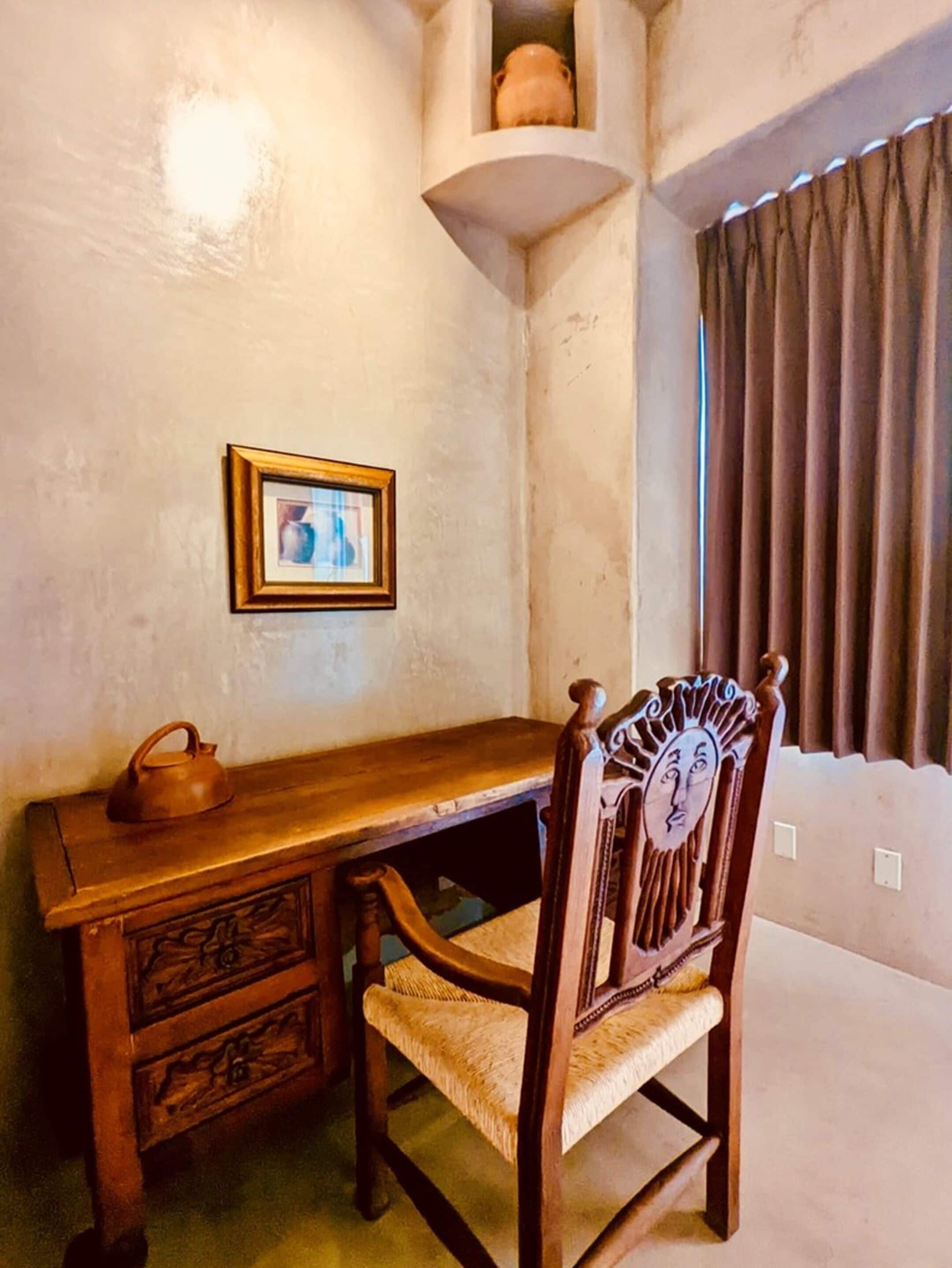 Un bureau en bois avec une chaise, un tableau encadré accroché au mur et une fenêtre avec des rideaux.