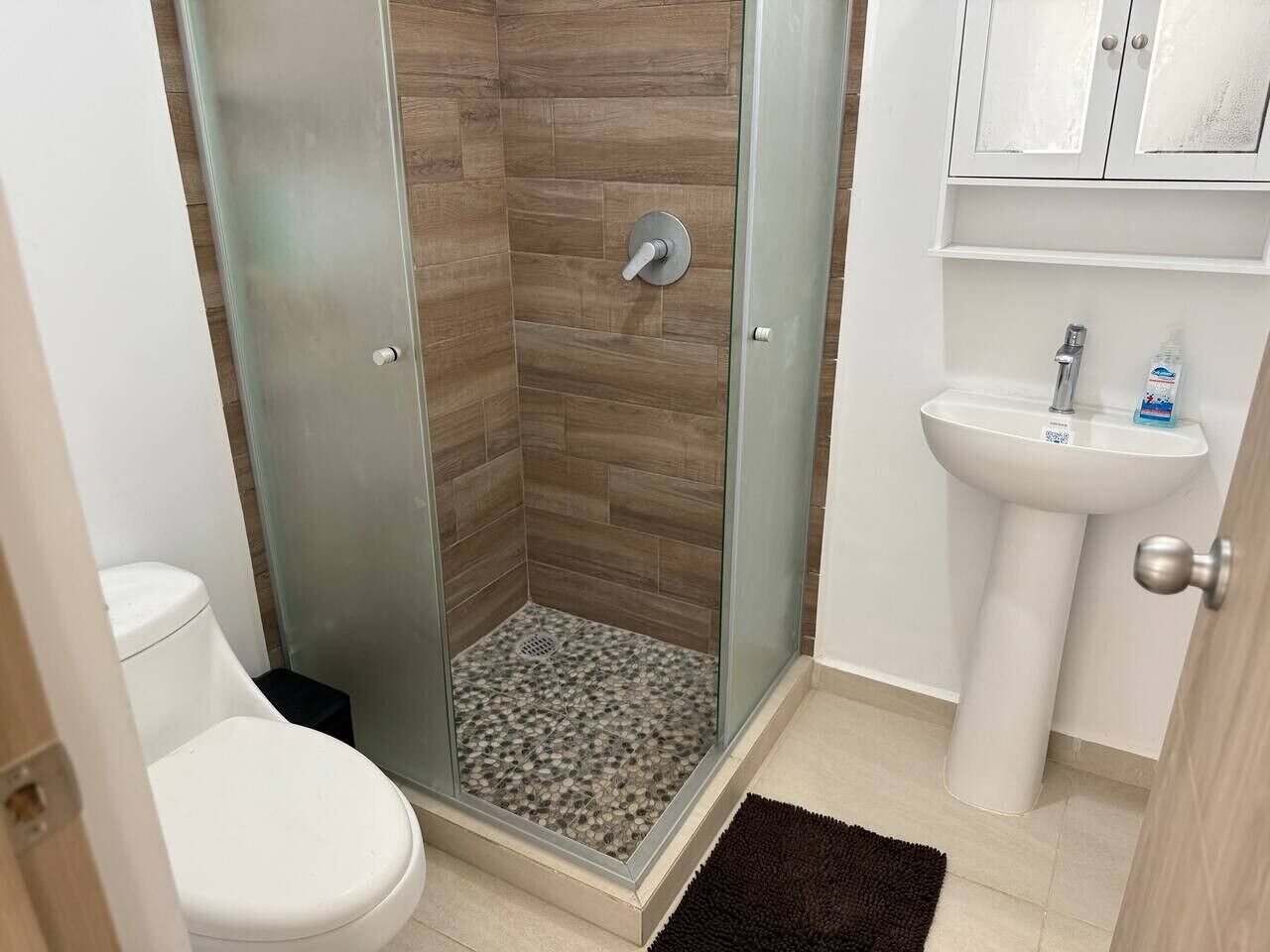 Ein Badezimmer mit einer gläsernen Dusche, einer weißen Toilette und einem Standwaschbecken.