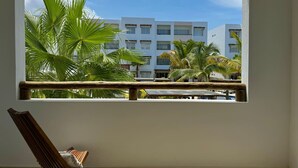A room with a large window overlooking a building with multiple floors and palm trees. - Almarena Apartments Coto Coral (Mazatlán)