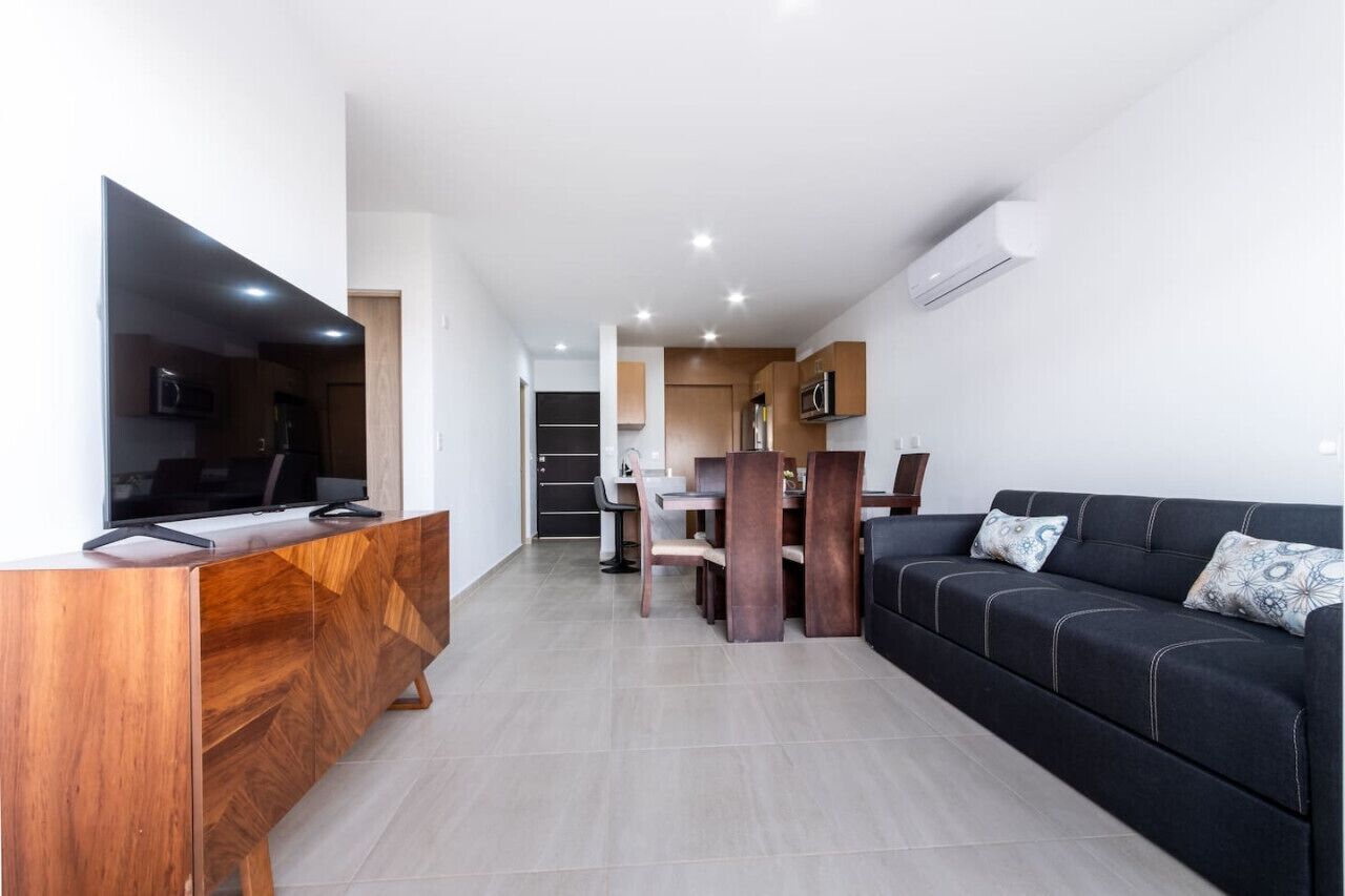 Un salon moderne avec un canapé noir, un meuble de rangement en bois et un coin repas comprenant une table et des chaises.