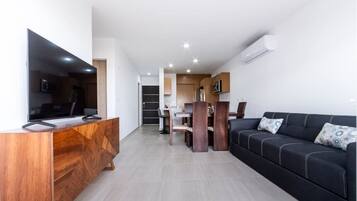 Un salon moderne avec un canapé noir, un meuble de rangement en bois et un coin repas comprenant une table et des chaises.
