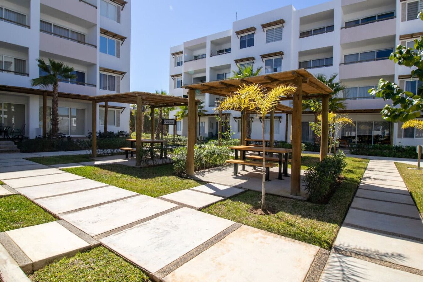 A courtyard with outdoor seating, palm trees, and a multi-story building in the background.