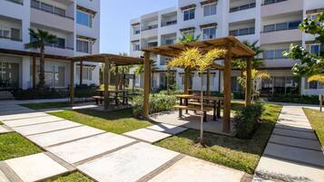 A courtyard with outdoor seating, palm trees, and a multi-story building in the background.