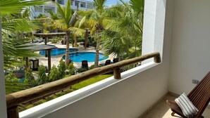A balcony with a view of a swimming pool, palm trees, and a white building in the background. - Almarena Apartments Coto Coral (Mazatlán)
