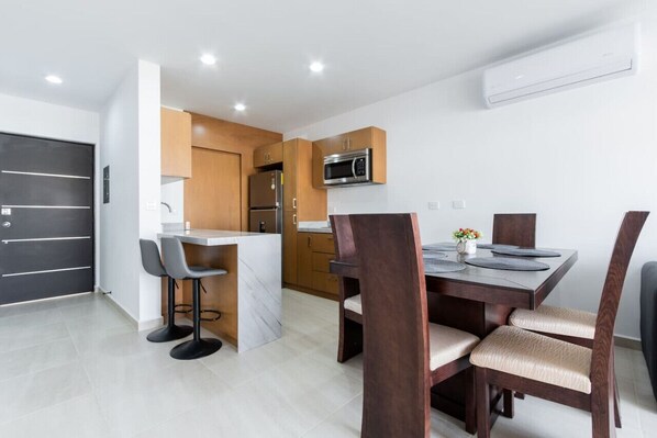 Una cocina moderna con microondas integrado, refrigerador y comedor con isla de mármol y sillas de madera.