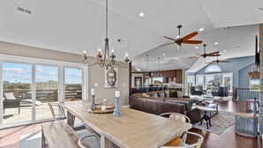 Amplia sala de estar con un gran comedor de madera, asientos cómodos, ventiladores de techo y vistas a través de puertas correderas de vidrio.
