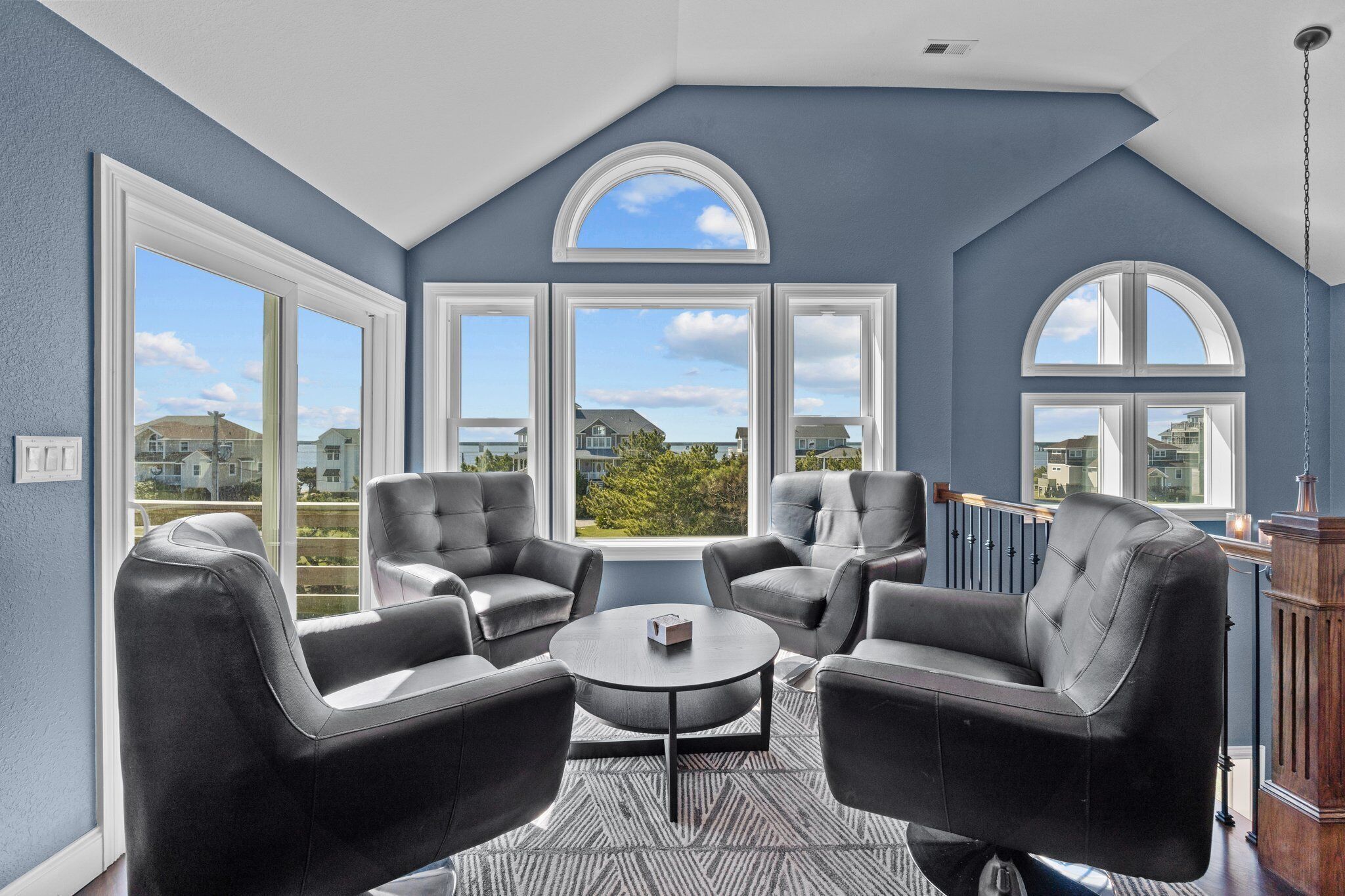 A room with large windows, leather chairs, a small table, and a view of houses.