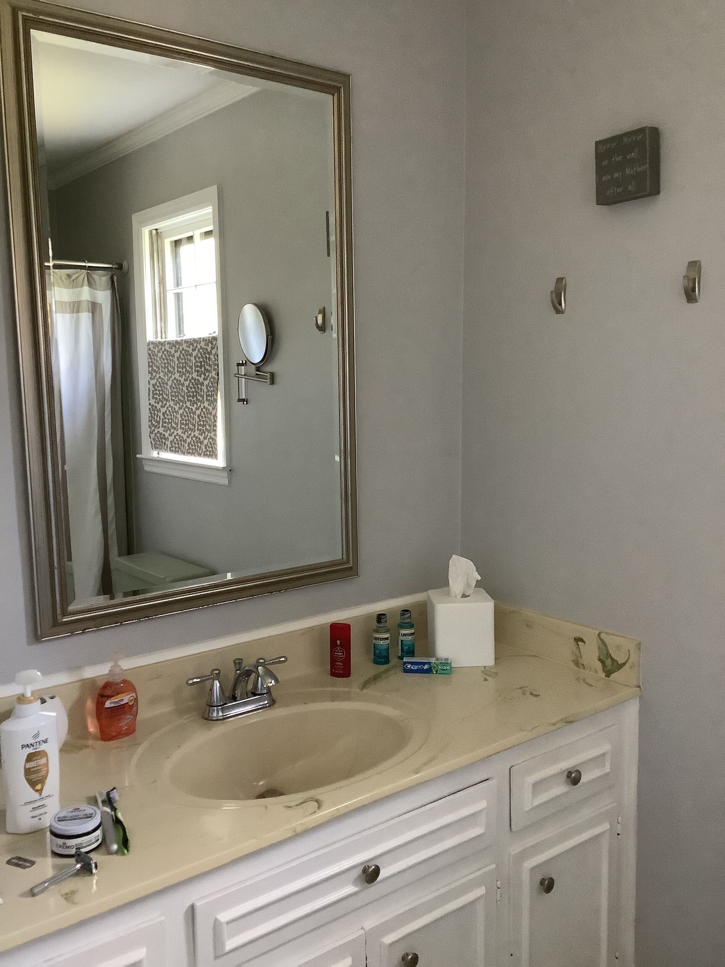 A bathroom with a large mirror, a sink, and a vanity with drawers. There are toiletries on the counter, including a soap dispenser, toothbrush, and toothpaste.