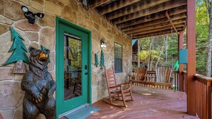 Une terrasse en bois avec un mur en pierre, une porte verte et une statue d’ours.